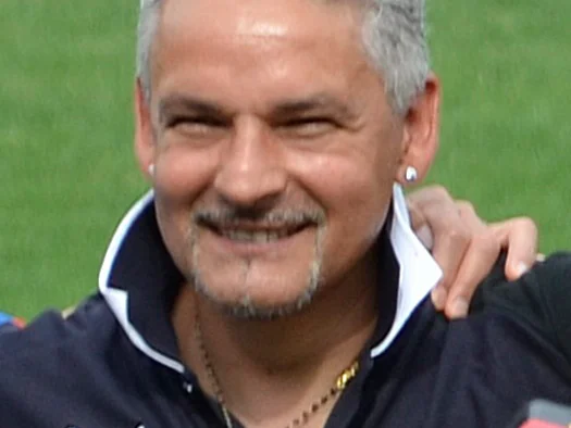 Roberto Baggio, gråhårig och leende, i mörk piké framför en gräsplan
