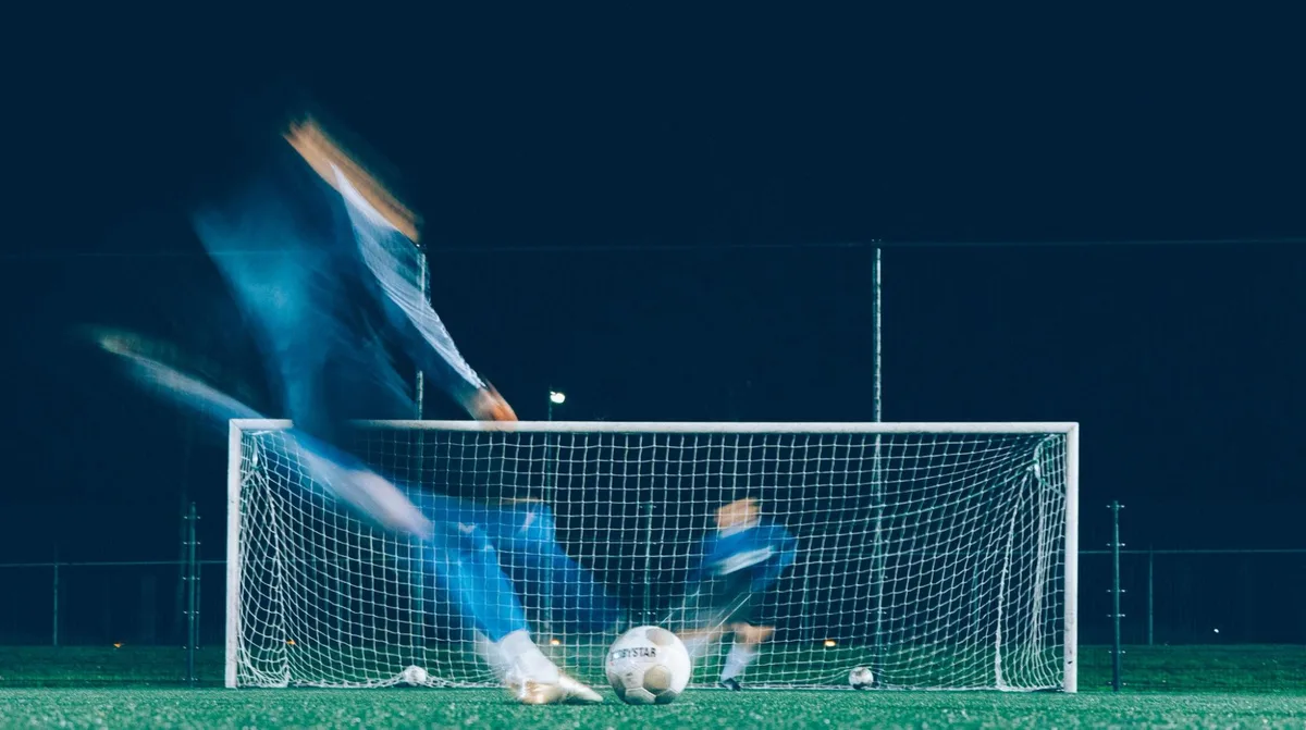 Målvakt i rörelse framför mål under kvällsmatch, fångad med rörelseoskärpa